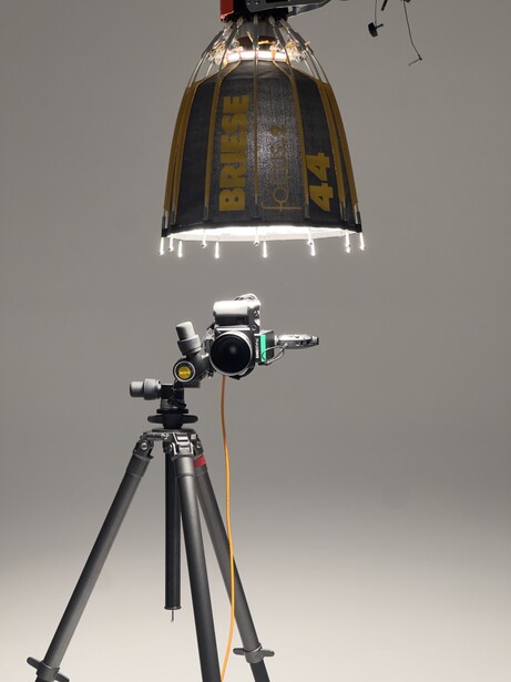 Studio lighting setup with a large parabolic softbox suspended above a camera mounted on a tripod.