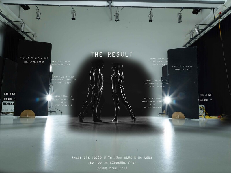 Gallery installation with two silhouetted figures standing beneath text reading 'THE RESULT' against spotlit backdrop.