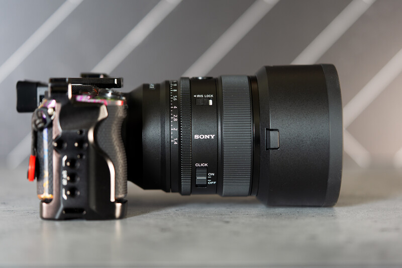 Sony mirrorless camera body with attached prime lens and red microphone mounted on top.