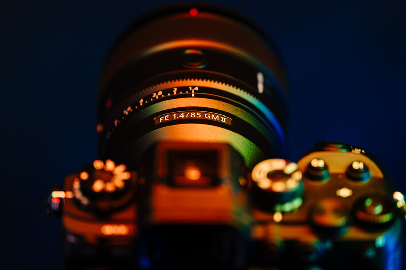 Vintage camera lens with focus ring and aperture markings, lit with warm orange and cool blue gel lighting against a dark background.