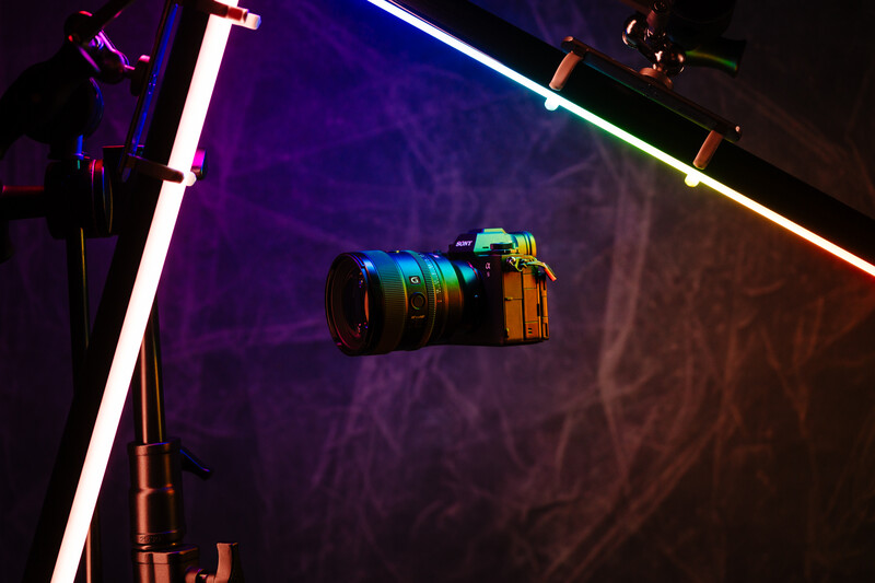 Camera suspended in front of colorful neon light tubes against a textured backdrop.