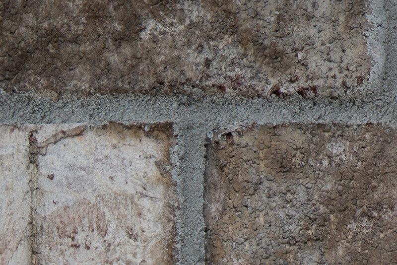 Close-up of weathered concrete surface with distinct tonal blocks and visible erosion patterns.