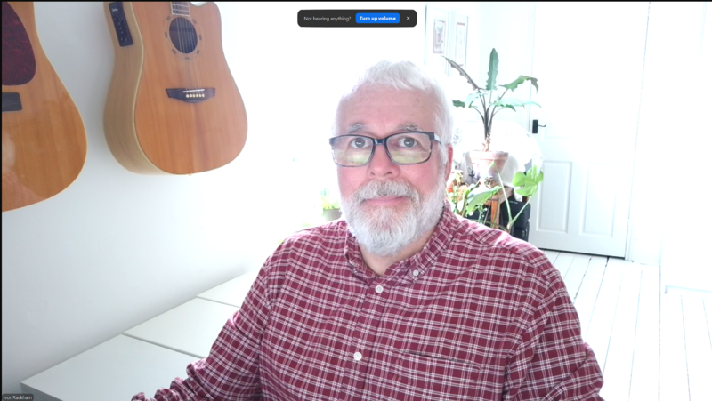 Older man with white hair and beard wearing glasses and red plaid shirt in home studio setting.