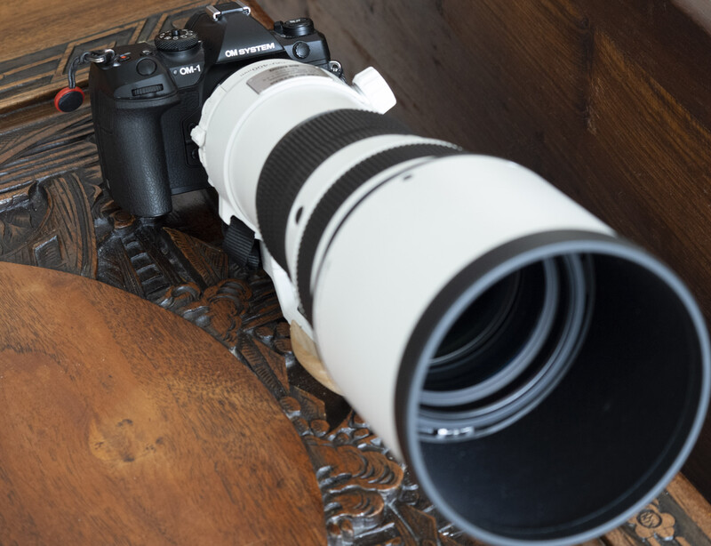 White telephoto lens mounted on black DSLR camera on wooden surface.