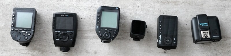 Six camera flash units arranged in a row on a concrete surface.