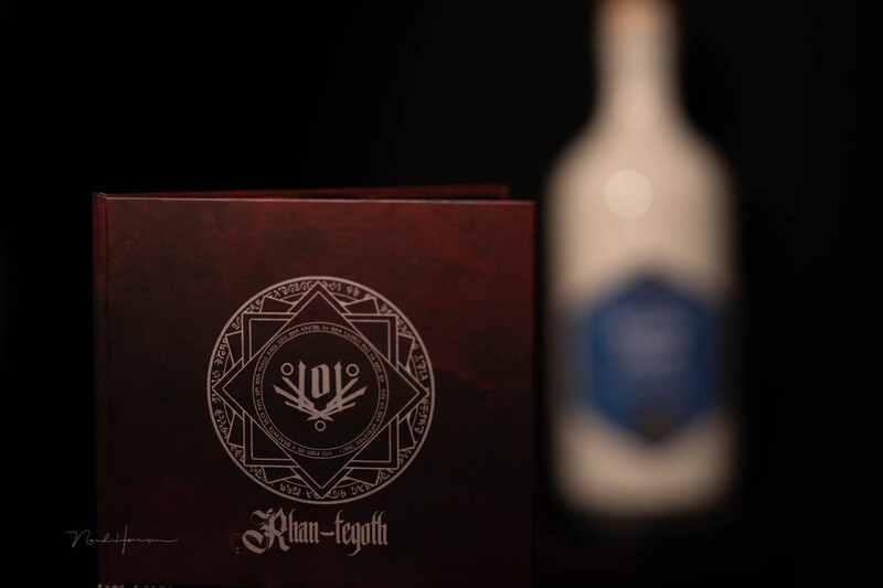 Dark red leather box with ornate circular geometric emblem and text, photographed next to a blurred wine bottle against black background.