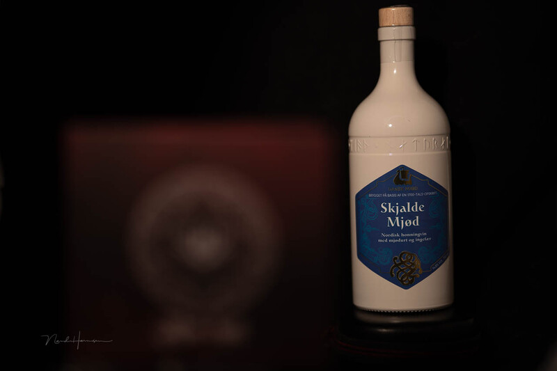 Bottle of Skjalde Mjød mead positioned against a dark, blurred circular background on black.