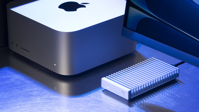 Mac mini computer next to an external SSD drive on a blue-lit desk surface.