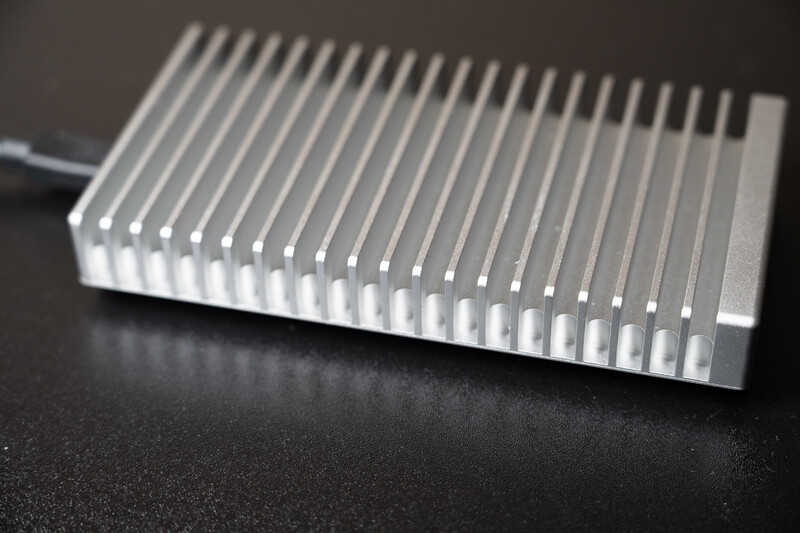 Aluminum heat sink with parallel fins and attached power cable on dark textured surface.