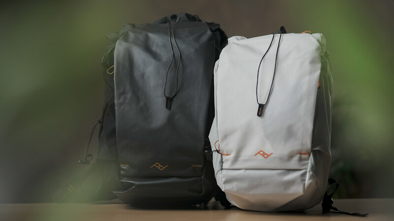 Black and white roll-top backpacks displayed side by side against a blurred green background.