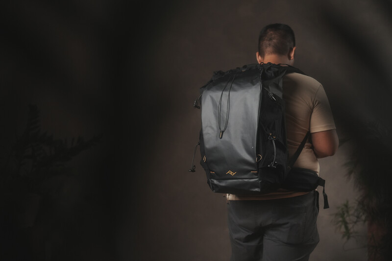 Person wearing a dark backpack photographed from behind against a muted background with dramatic side lighting.