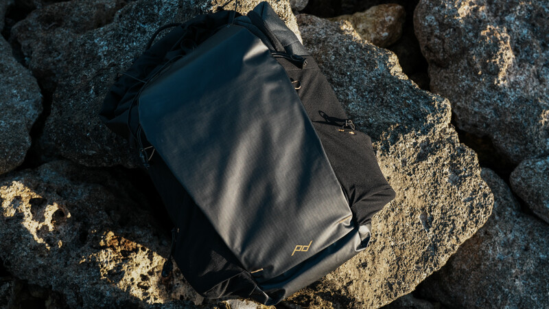 Black camera backpack resting on large granite boulders in bright sunlight.