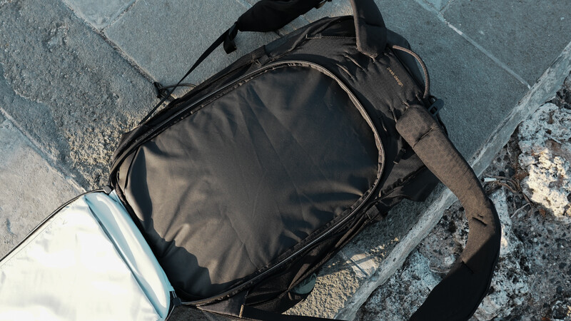 Black camera bag with shoulder strap lying on weathered stone pavement.