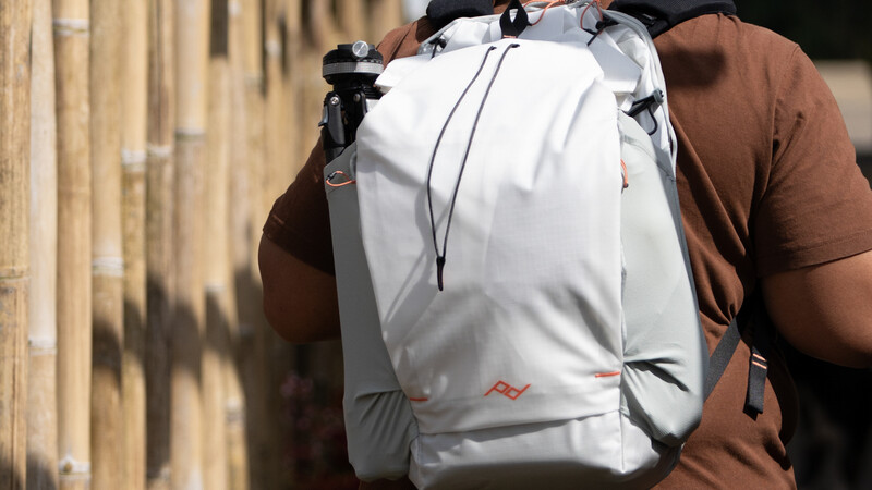 Person wearing a white backpack with black straps and chest harness over a brown shirt.