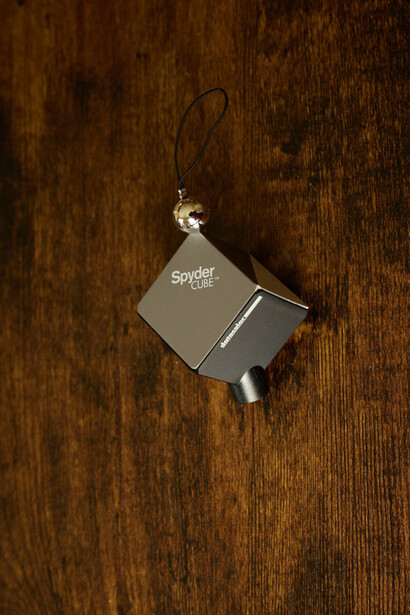 Overhead view of a small gray Spider camera hanging from a wire against a dark wood surface.