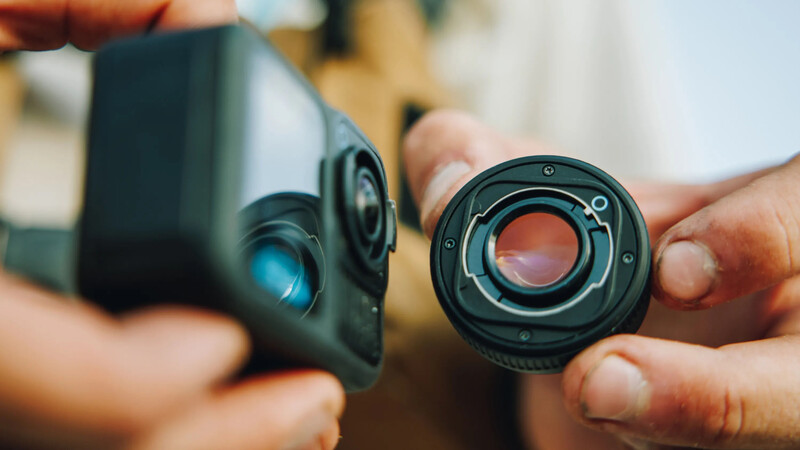 Close-up of a thermal imaging camera lens being held in hand, showing the optical glass element and metal housing.