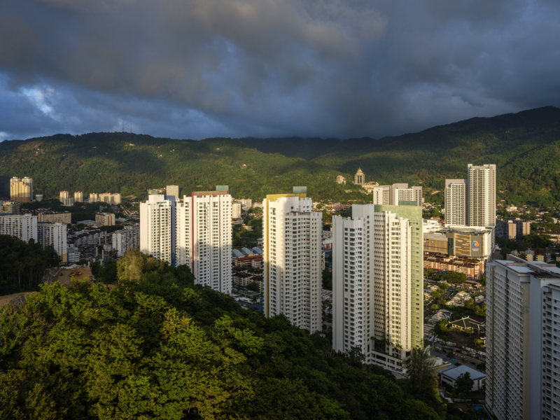 Residential high-rise apartment buildings with forested mountains in background under dramatic storm clouds.