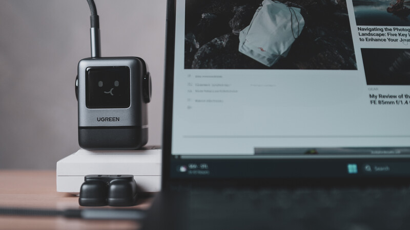 Ugreen USB hub with charging cables on white stand next to laptop displaying photography website.
