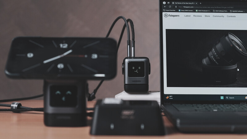Photography workspace with smartwatch, smartphone displaying time, monitor showing lens image, and camera equipment on desk.