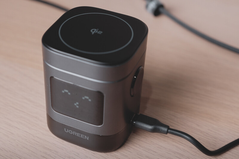 Ugreen portable power station with black top panel and gray cylindrical body sitting on wooden surface with cable attached.