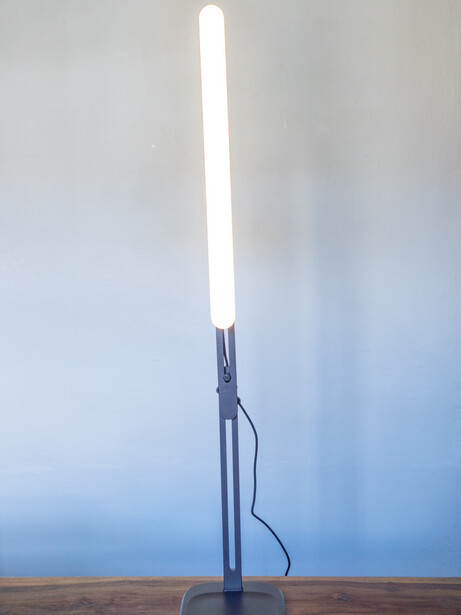 Tall cylindrical LED tube light with glowing white top section and dark metal base on wooden surface.