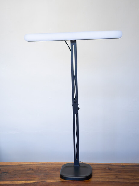 Modern LED desk lamp with thin white tube light on black telescoping stand with round weighted base.