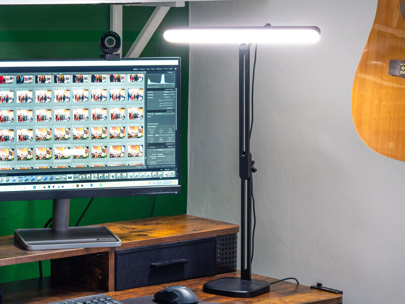 Photography editing workspace with dual monitors displaying contact sheets and color-corrected images under bright LED panel lighting.