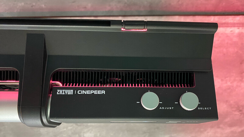 Close-up of a Zhiyun Cinepeer camera stabilizer control panel with adjust and select knobs against pink backdrop.