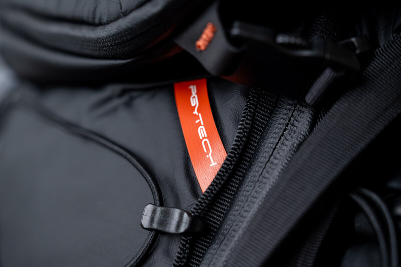 Close-up of a camera bag with red and black nylon fabric and orange accent label on zipper.