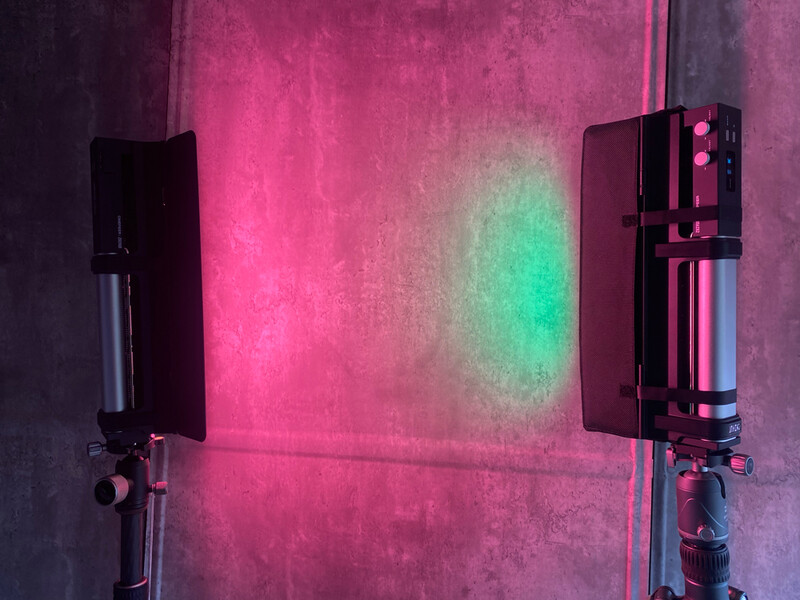 Two professional LED panel lights mounted on tripods against a textured wall, emitting vibrant pink and green colored light.