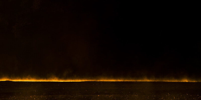 Golden light glow on dark horizon at night with scattered lights below.
