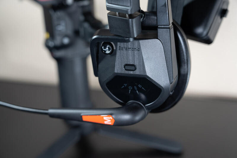 Close-up of a gaming headset with gray and black ear cup, visible microphone boom with orange accent, and cables in sharp focus.