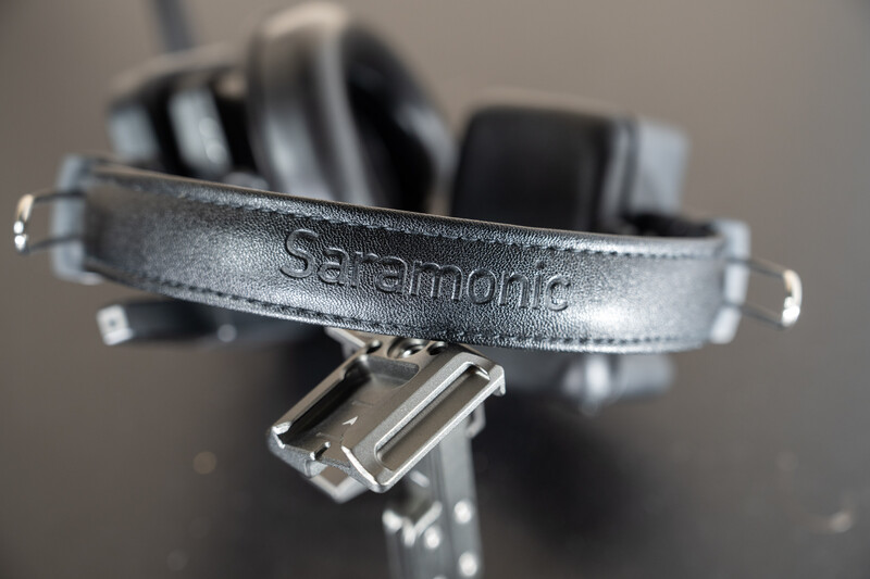 Close-up of a Saramonic microphone headband with metal clasp and cable connector against blurred headphones.