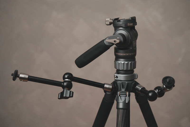 Professional fluid head tripod with telescoping legs and counterbalance arm against neutral background.