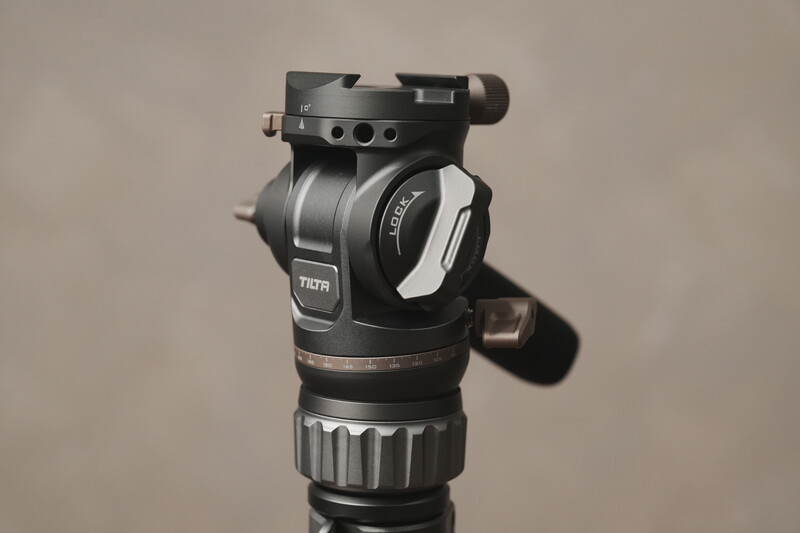 Professional fluid head tripod mount with counterbalance system and quick-release plate against neutral background.