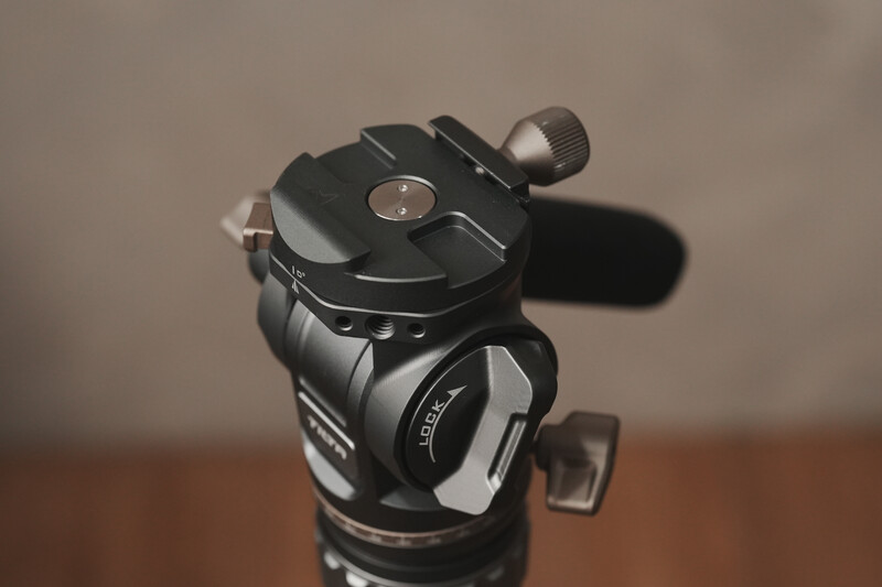 Professional fluid head tripod with panoramic pan-tilt mechanism mounted on wooden surface.