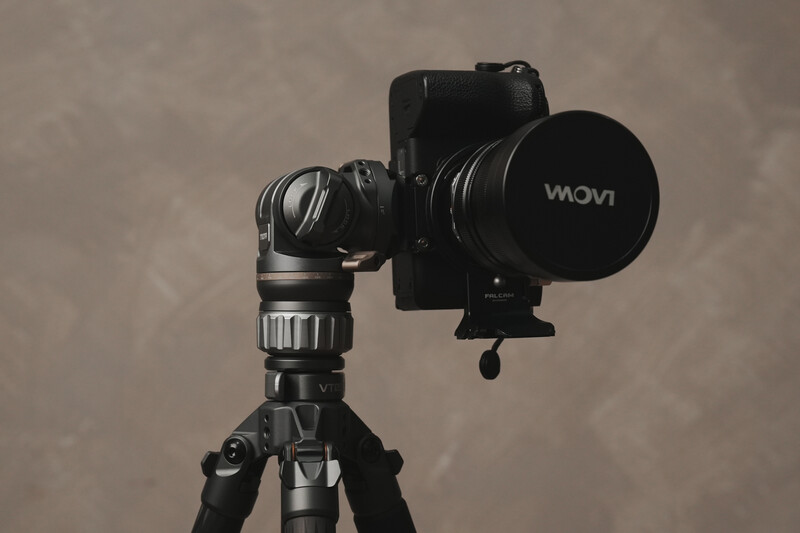 Professional gimbal stabilizer with mounted camera and telephoto lens on tripod against neutral backdrop.