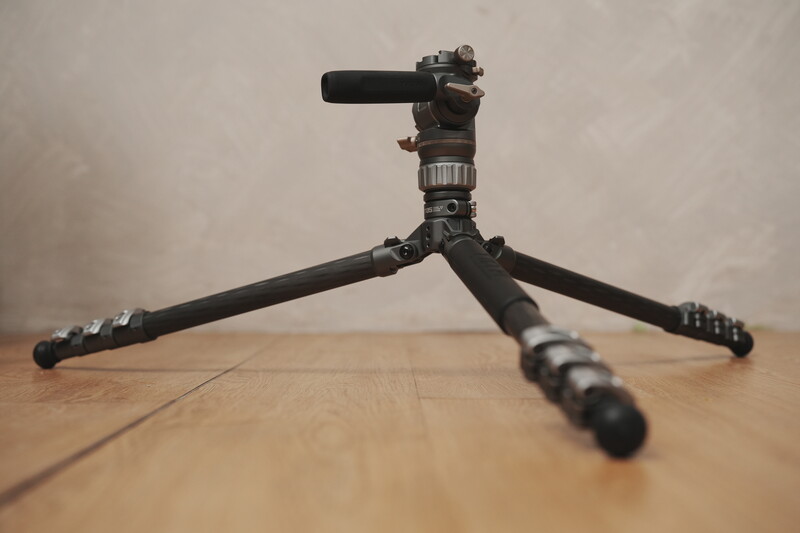 Professional tripod with fluid head and microphone attachment on wooden floor.