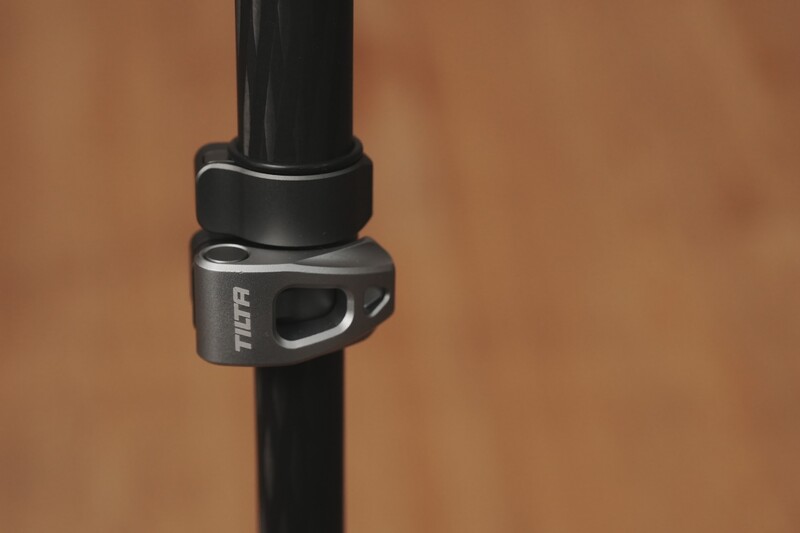 Close-up of a gray and black camera strap clamp attachment mounted on a black pole against a tan background.