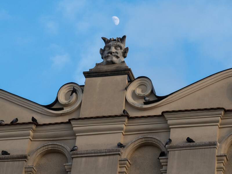 Stone gargoyle sculpture mounted on classical building pediment with scrolled ornaments.