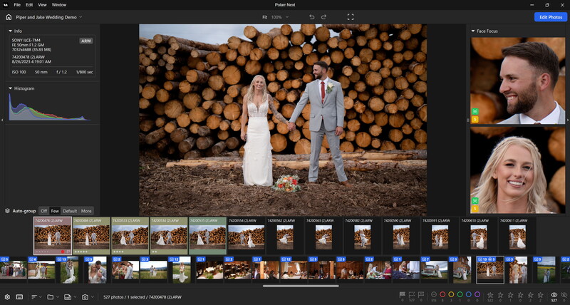 Bride and groom standing hand-in-hand in front of a large stack of stacked logs during outdoor wedding portrait session.
