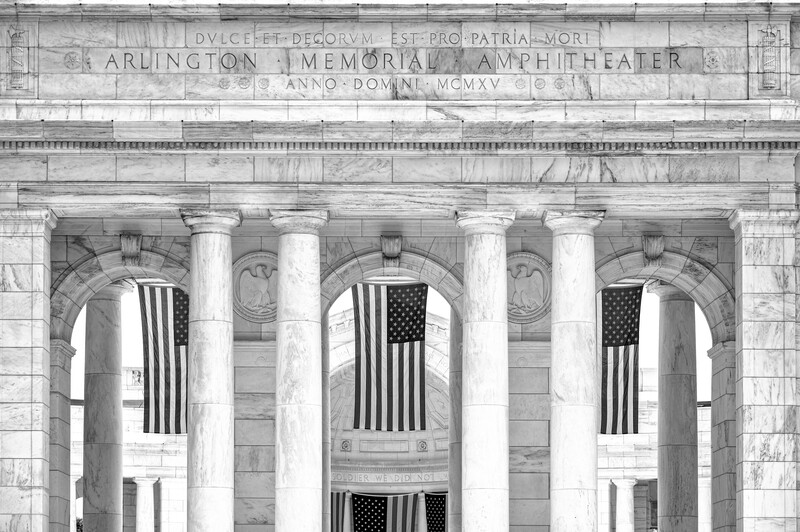 Classical marble columns with American flags hanging between them at a memorial amphitheater entrance.