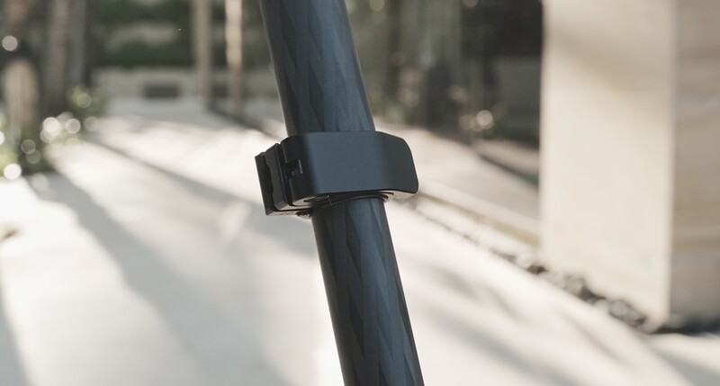 Black cable clip mounted on a vertical dark pipe with blurred interior hallway in background.