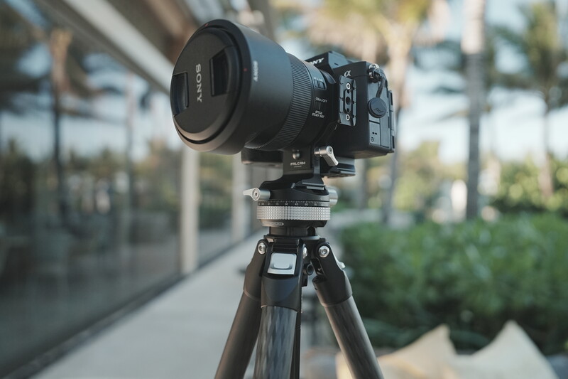 Professional cinema camera with telephoto lens mounted on tripod in outdoor urban setting.