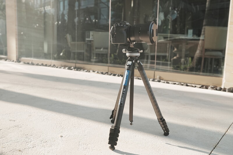 Professional tripod with fluid head and smartphone mount set up on a concrete surface in front of a modern glass storefront.