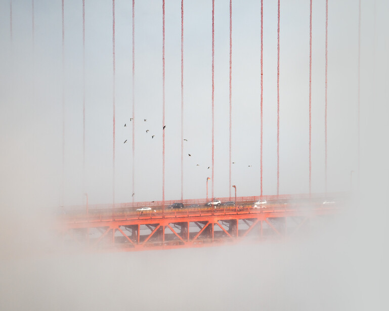 Golden Gate Bridge partially obscured by thick fog, with suspension cables visible and vehicles crossing the roadway.