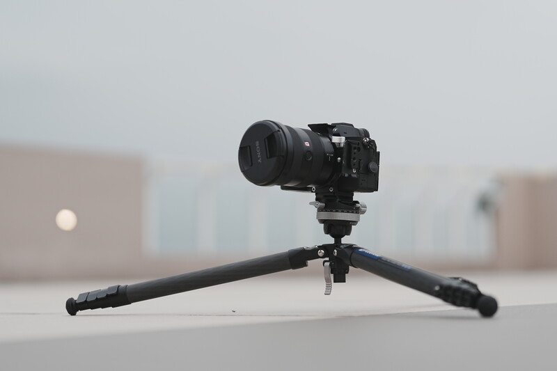 Professional DSLR camera mounted on a tripod with extended arms, positioned outdoors against a blurred urban backdrop.