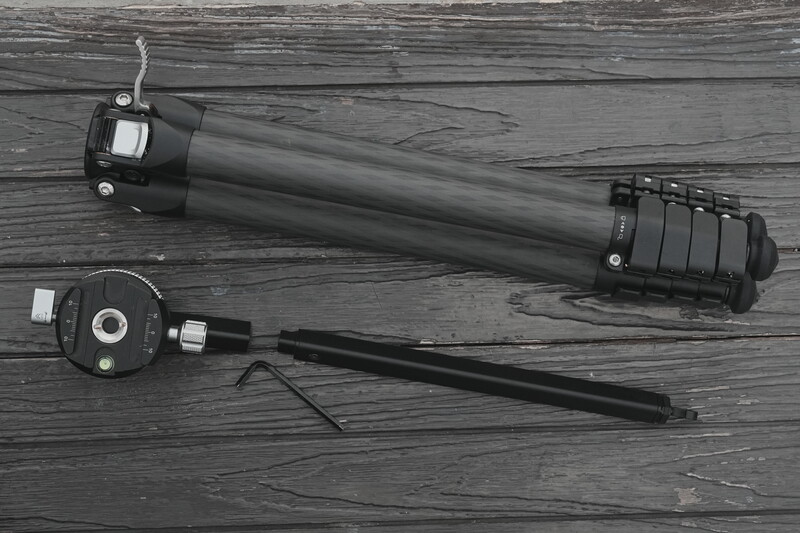 Monochrome flat lay of a camera slider, ball head, and extension arm on weathered wood.