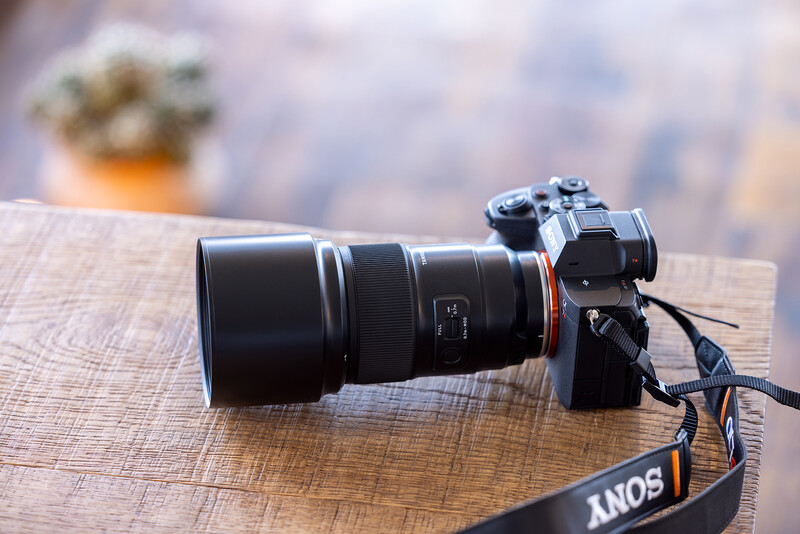 Sony mirrorless camera with telephoto lens mounted on wooden surface with camera strap visible.