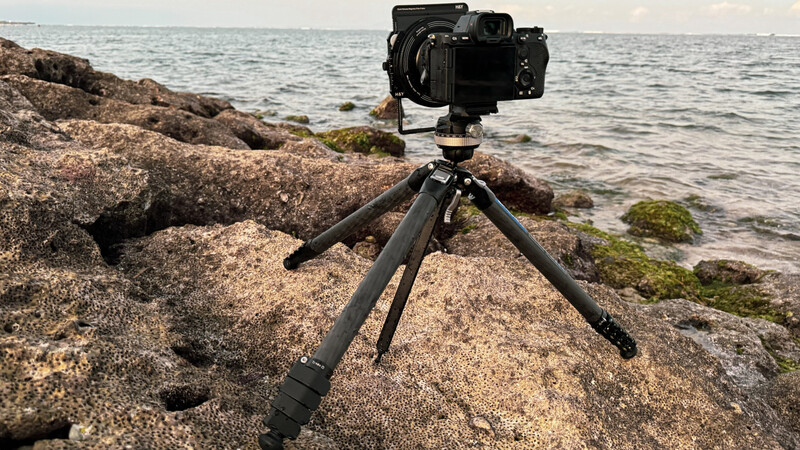 Professional mirrorless camera mounted on tripod positioned on rocky coastal terrain overlooking the sea.